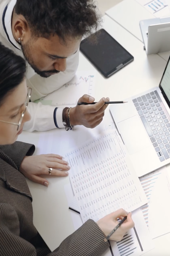 Two people are in an office examining a piece of paper with data printed on it