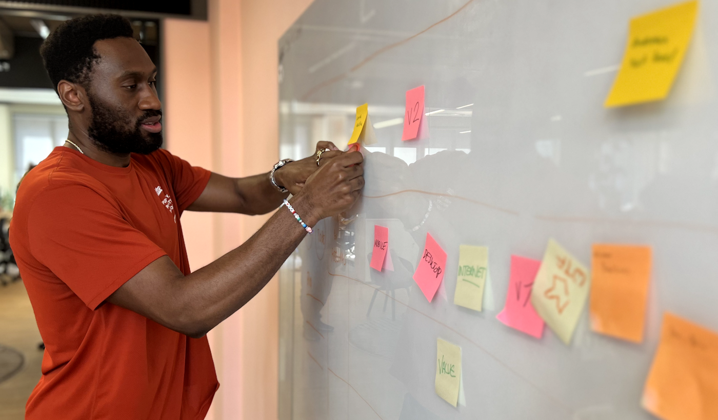 A man stands at a whiteboard to map out ideas that are written down on post-it notes.