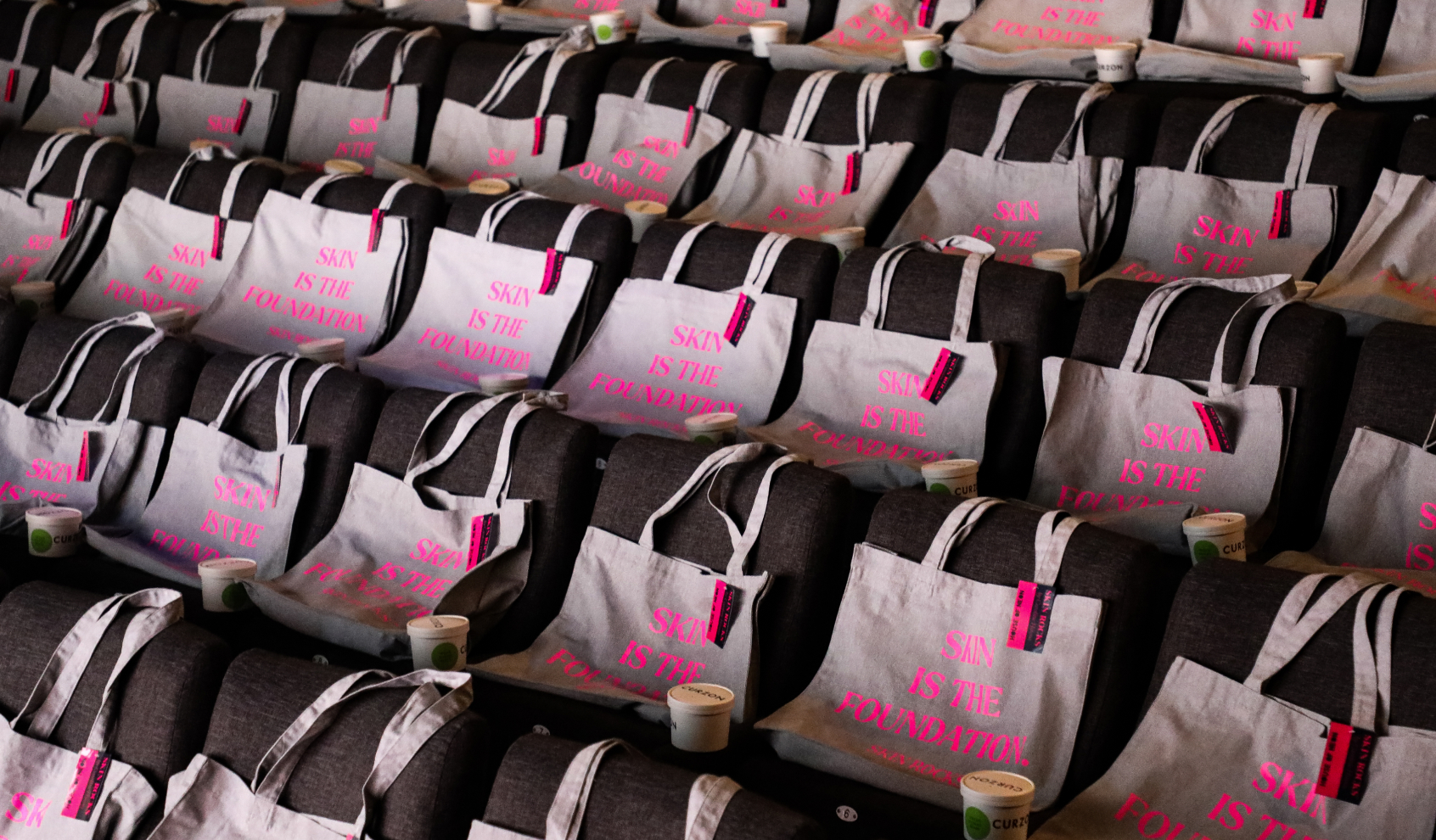 Rows of auditorium seats with white tote bags and small cups placed on each seat.