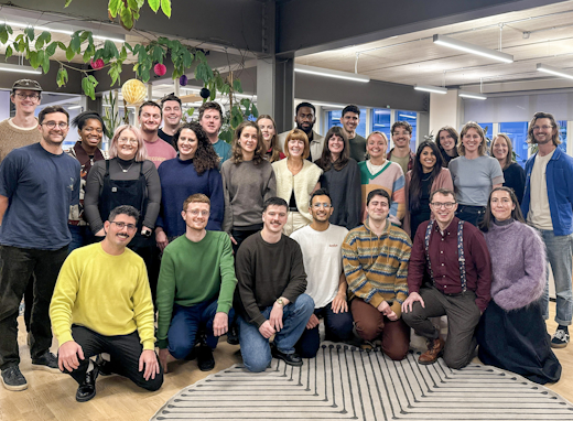 A team smiling in an office, with plants and modern lighting in the background.