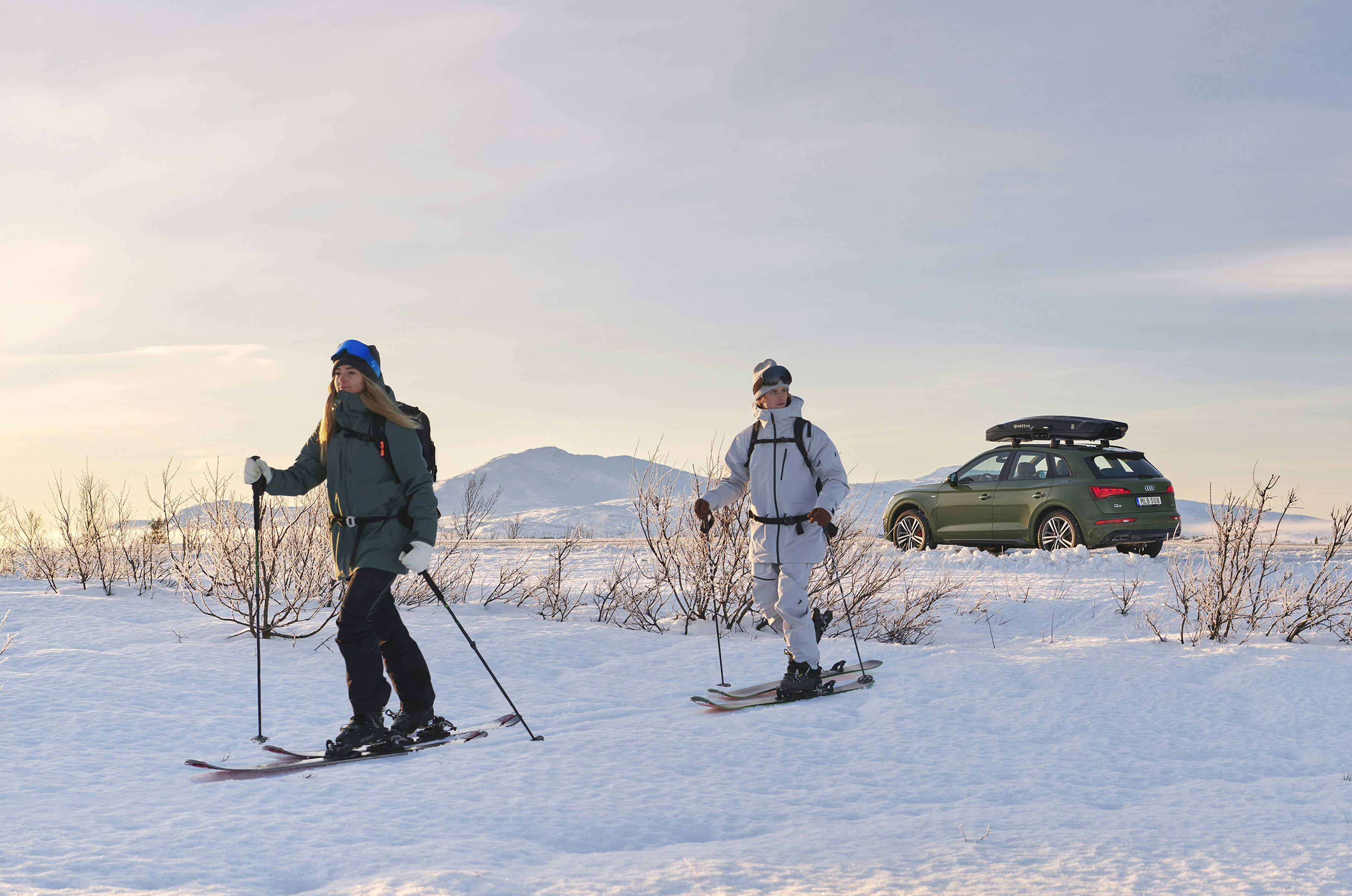 Two people skiing in front of a car