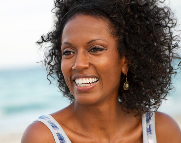 woman with black short curly hair on the beach in a tank top