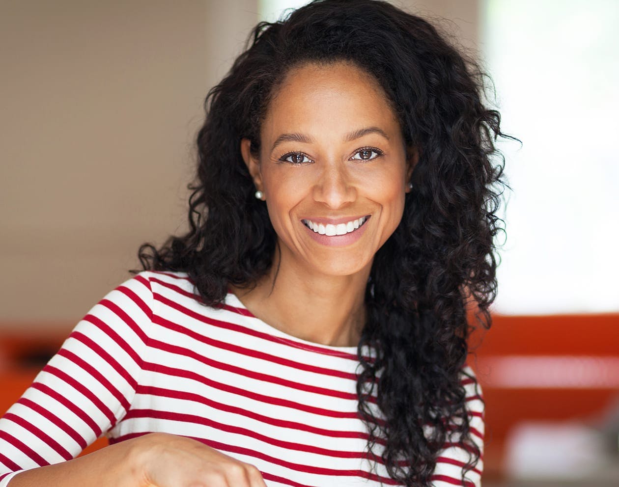 woman with long dark curly hair smiling in a white and red stripped shirt