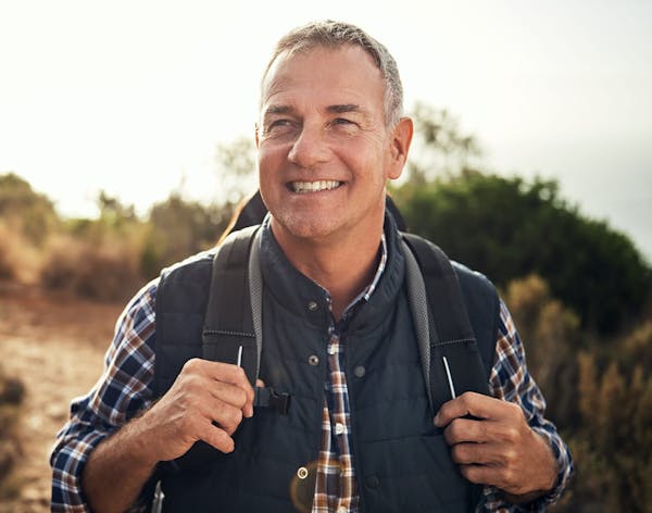 an older man smiling wearing a vest and backback