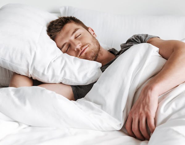 a man sleeping in a bed with white sheets