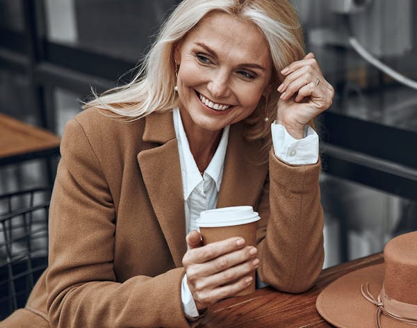 a blonde woman smiling in a white buttondown and brown blazer