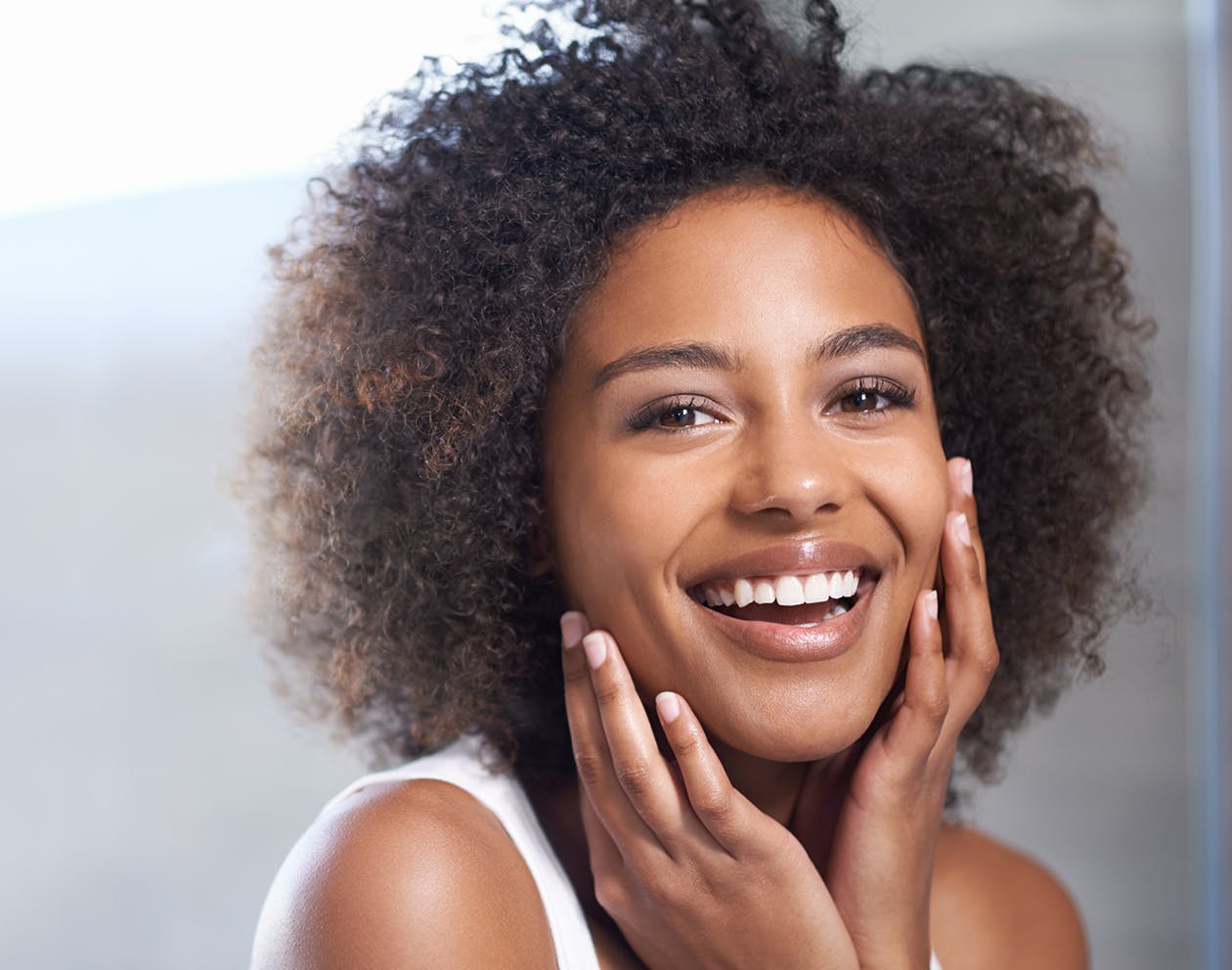 woman with dark curly hair smiling with her hands up toward her face