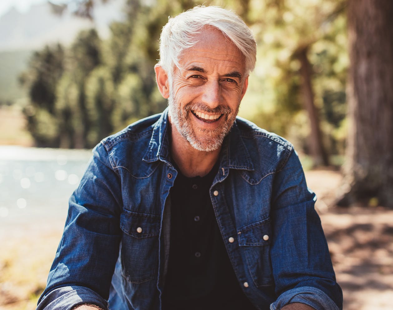 older man with grey hair in a denim shirt sitting outside