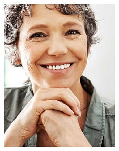 older woman smiling with her chin resting on her hands