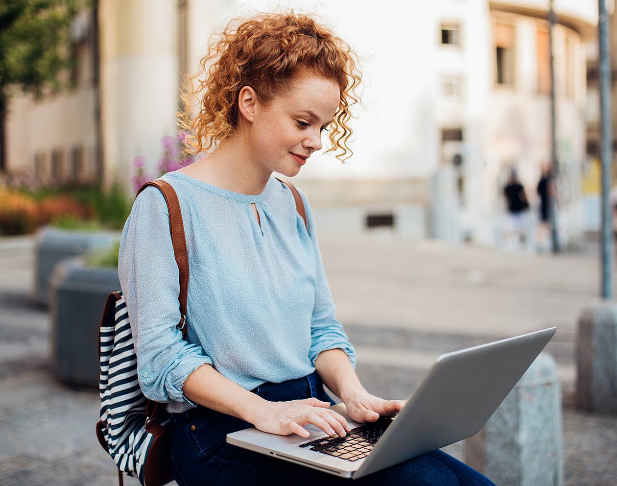 red haired woman sitting outside on her laptop