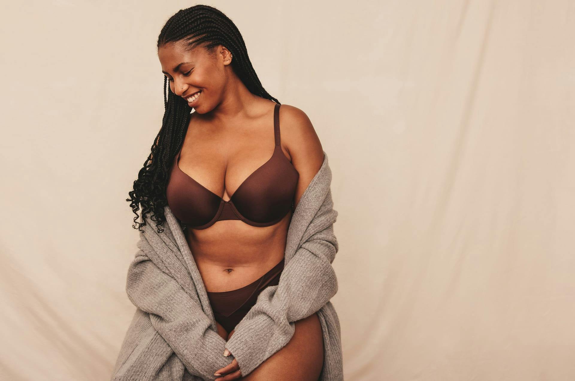 Woman in her underwear and a robe half on, looking down to the side and smiling