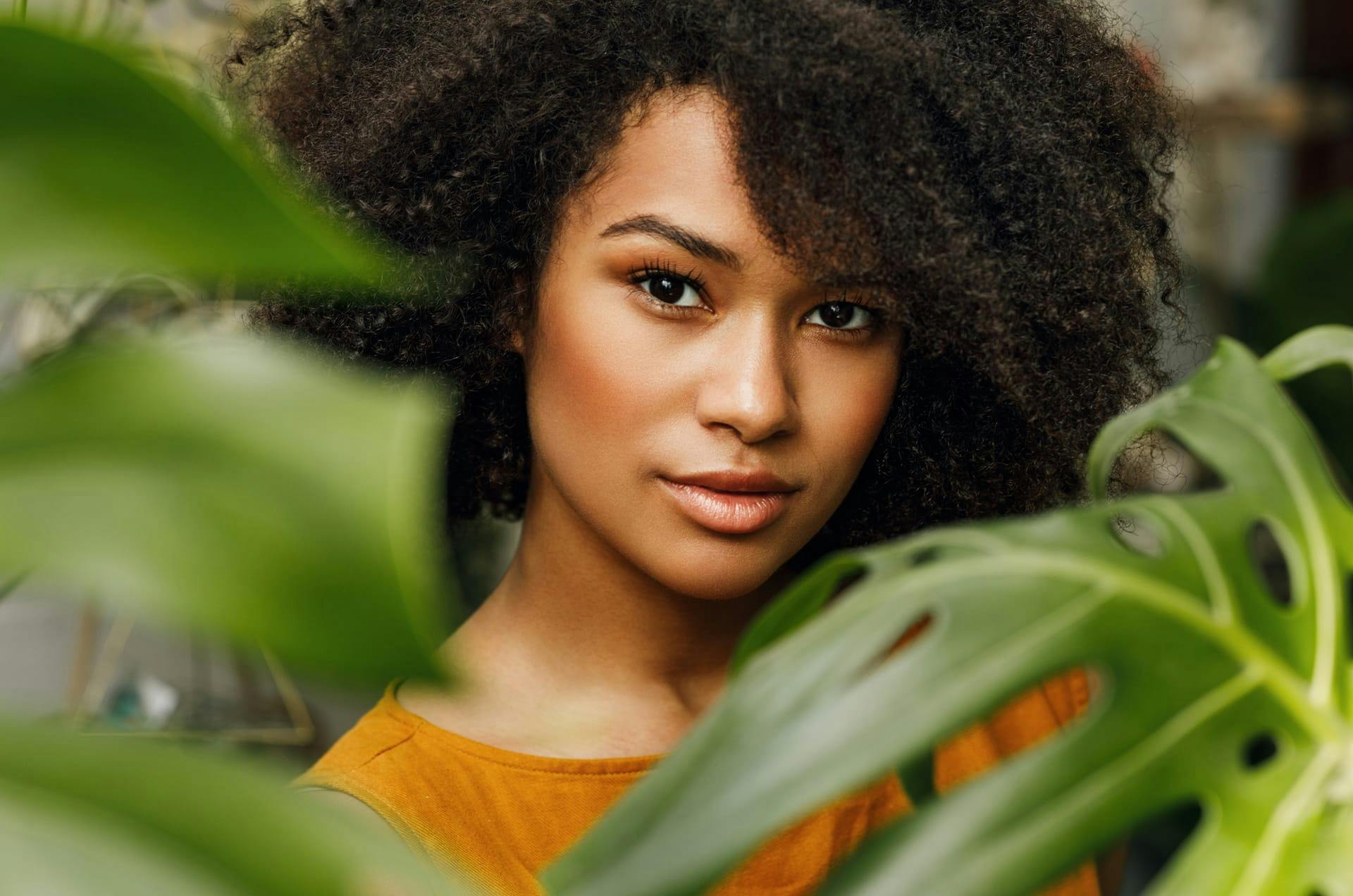 Woman with curly black hair behind some plant leaves