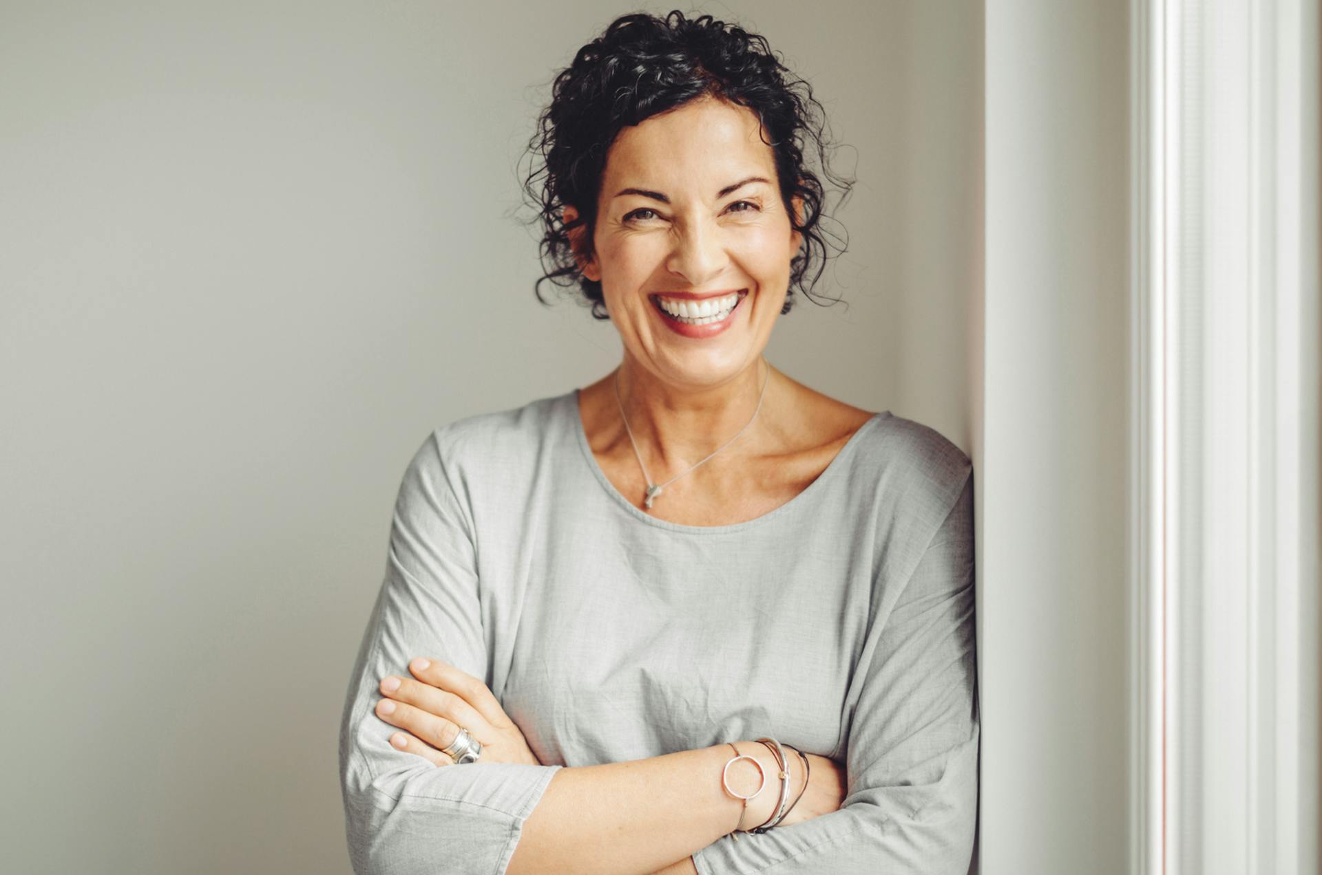 Older woman leaning against a wall with her arms crossed