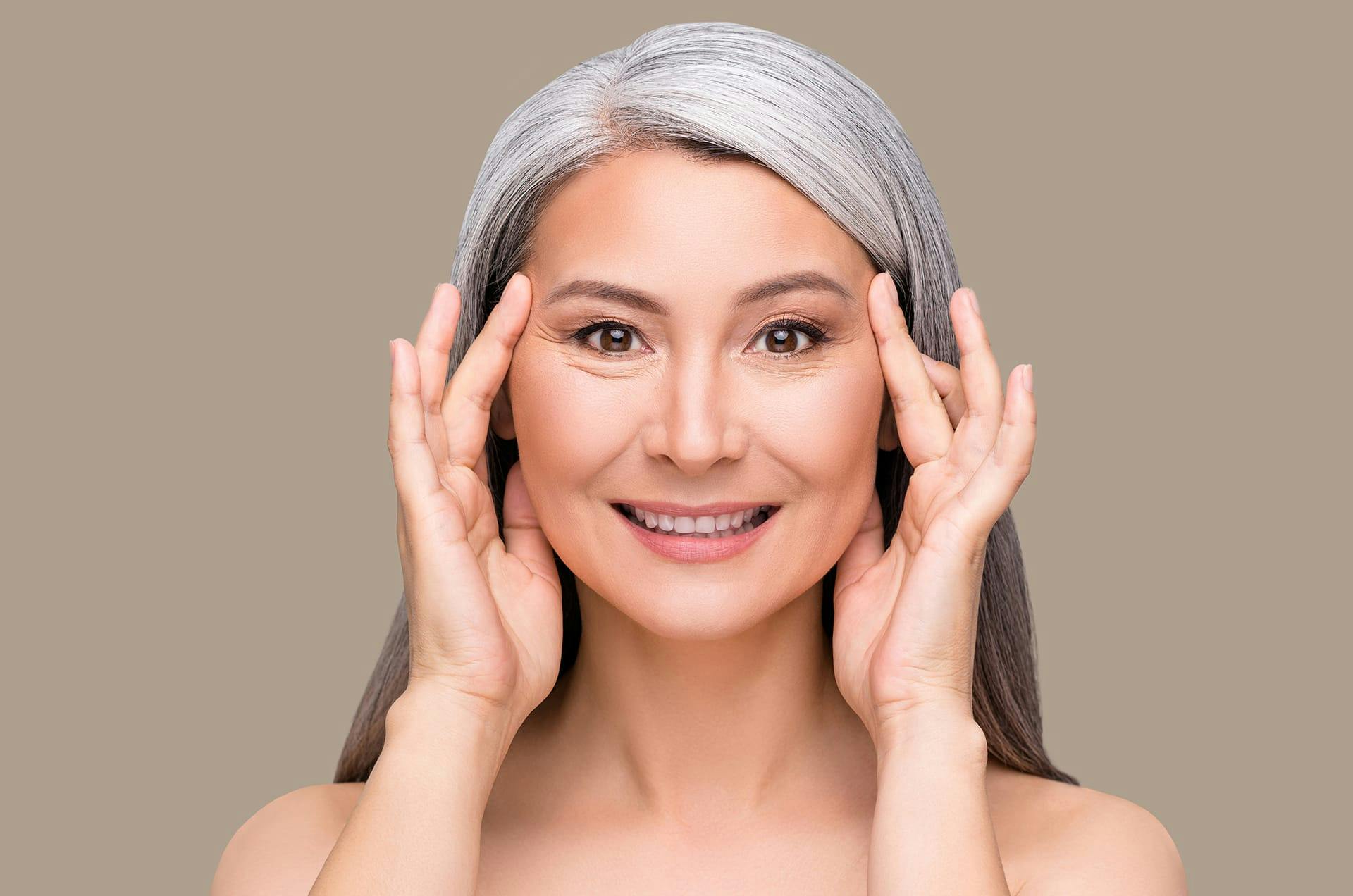 Woman with gray hair holding both hands to her face