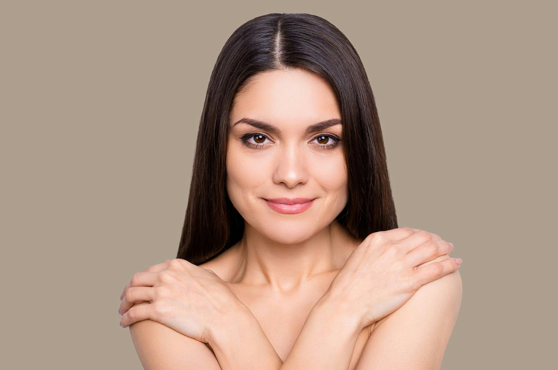 Woman with dark hair crossing her arms and her hands on her shoulders.