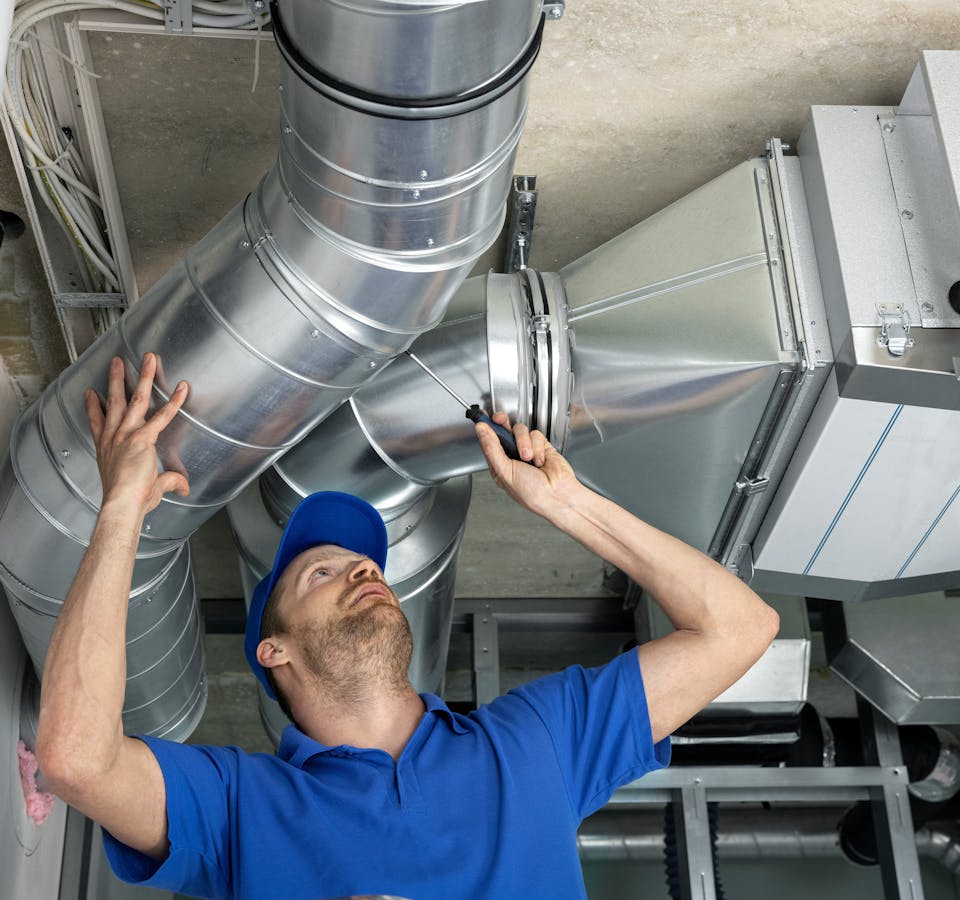 un travailleur installe un système de tuyaux canalisés pour la ventilation et la climatisation
