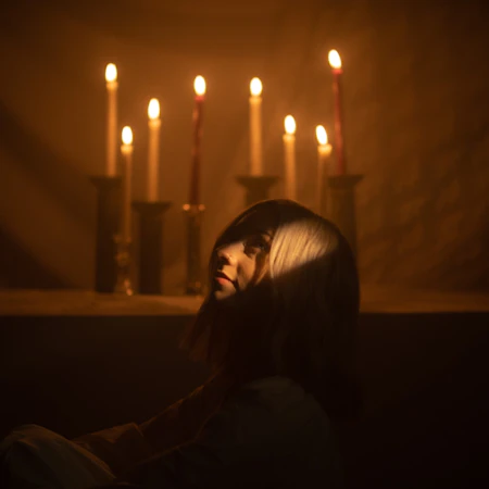 Tiffany looking up, seated in front of a table adorned with eight lit candles