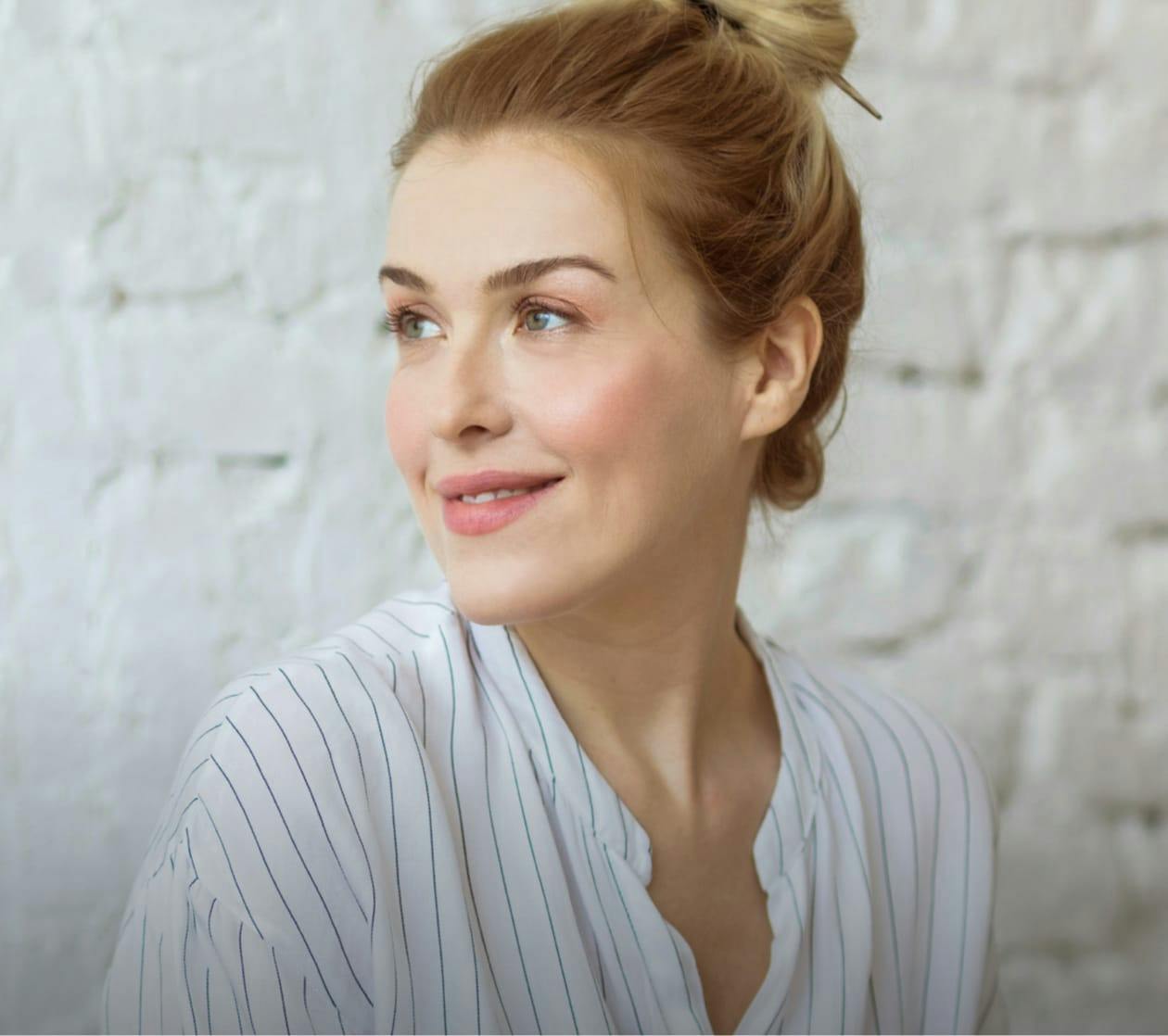 Beautiful blonde woman looking content in front of a white brick wall.