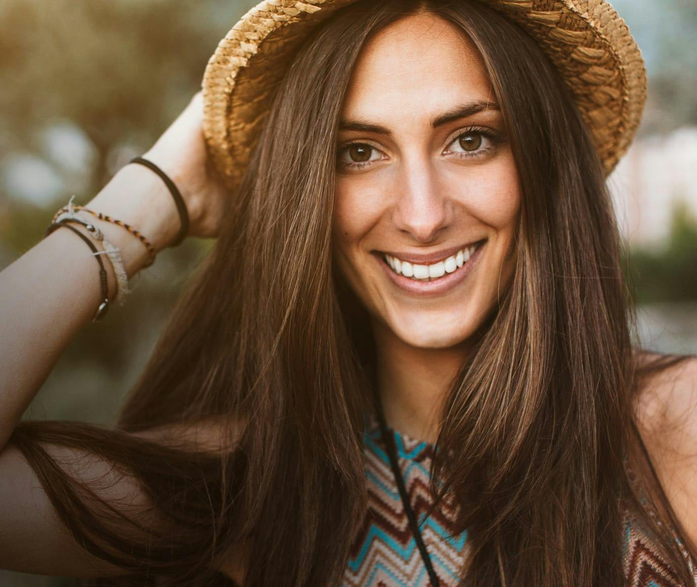 Beautiful woman with long, straight, brown hair, wearing a hat and smiling into the camera.