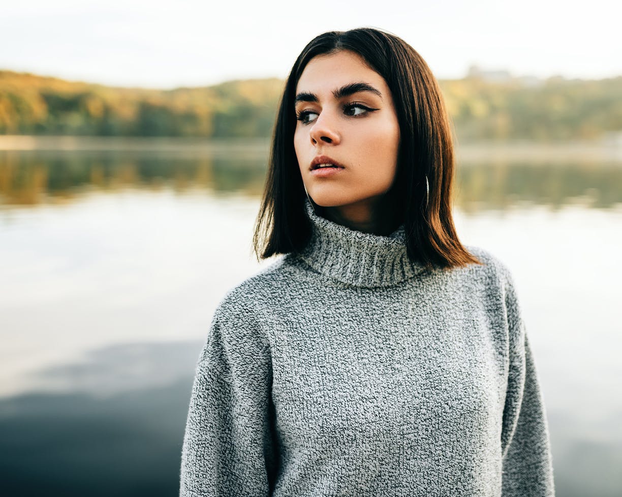 Short brown-haired woman in a grey sweater in front of a lake