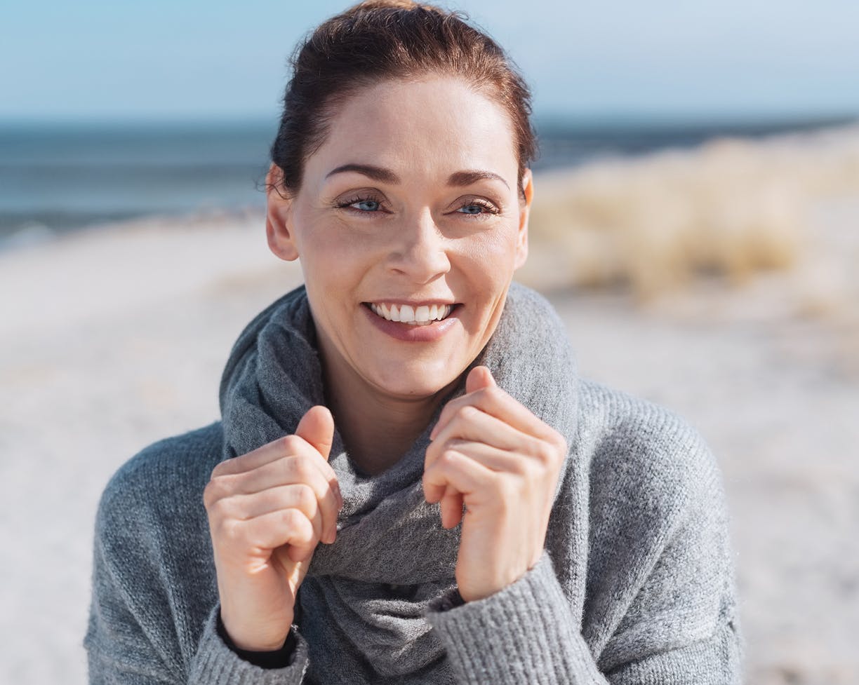 Middle-aged woman wearing a grey sweater at the beach