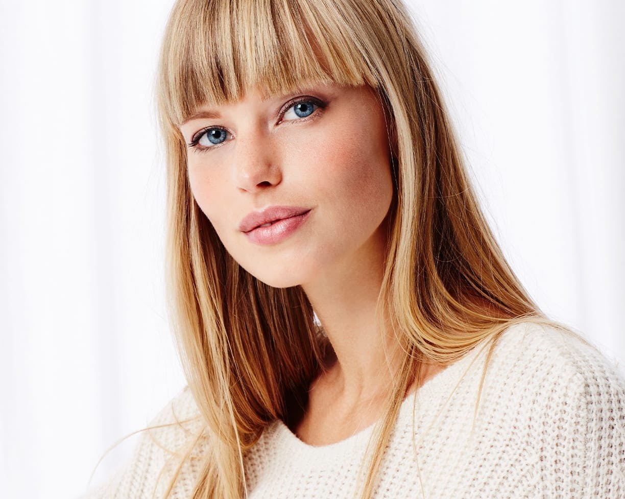 a blonde woman with blue eyes wearing a white knitted sweater