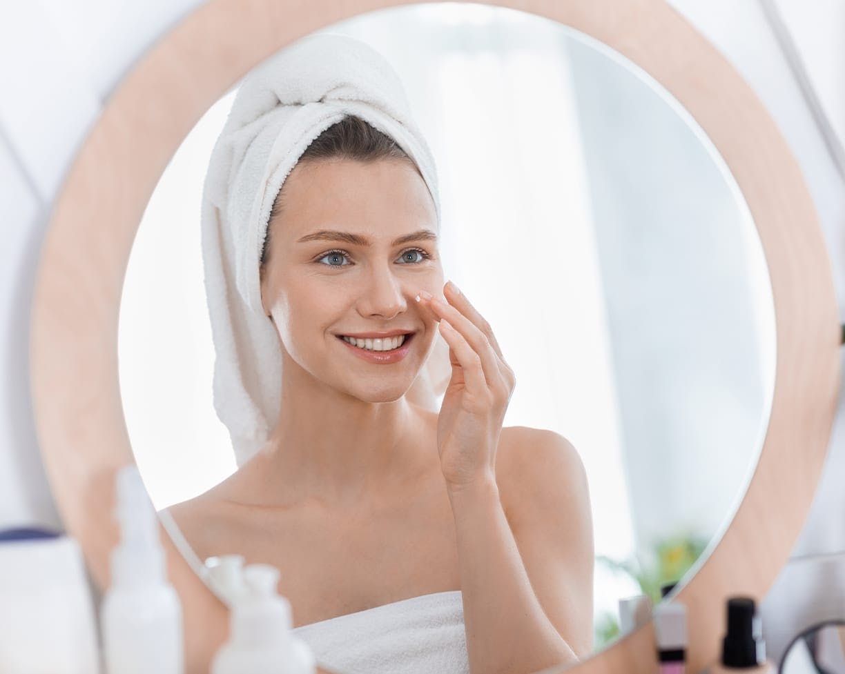 a woman looking into a mirror with a white towel on her head and around her body