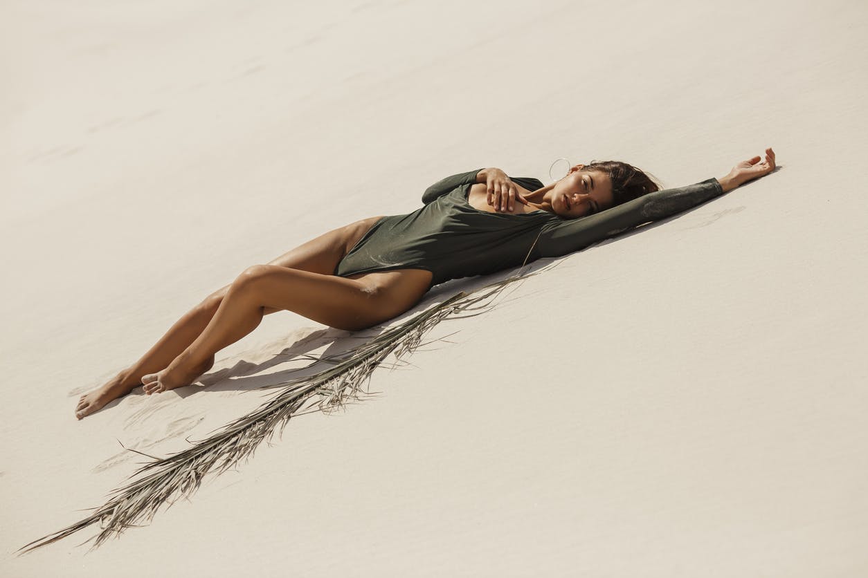 Woman laying on a hill of sand in a green body suit