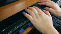 Close-up van twee handen die gebruik maken van een computer met braille display of braille toetsenbord