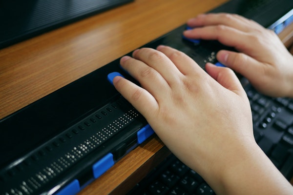 Close-up van twee handen die gebruik maken van een computer met braille display of braille toetsenbord