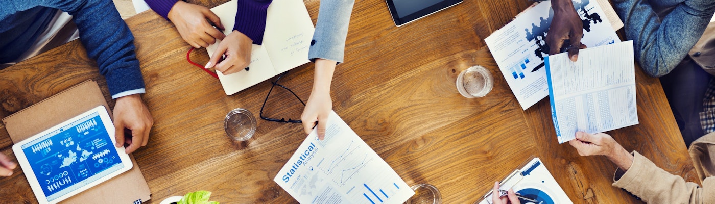bovenaanzicht van personen in overleg aan een tafel met laptops en papieren