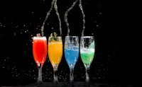 Vier glazen met van links naar recht een rode, gele, blauwe en groene drank