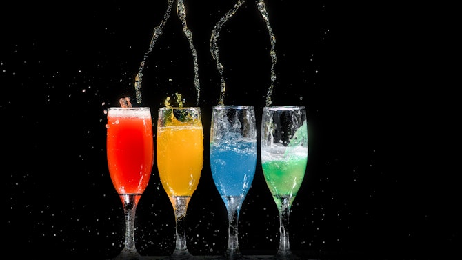 Vier glazen met van links naar recht een rode, gele, blauwe en groene drank