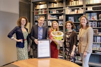 5 personen voor een boekenkast met bloemetje en ondertekend document