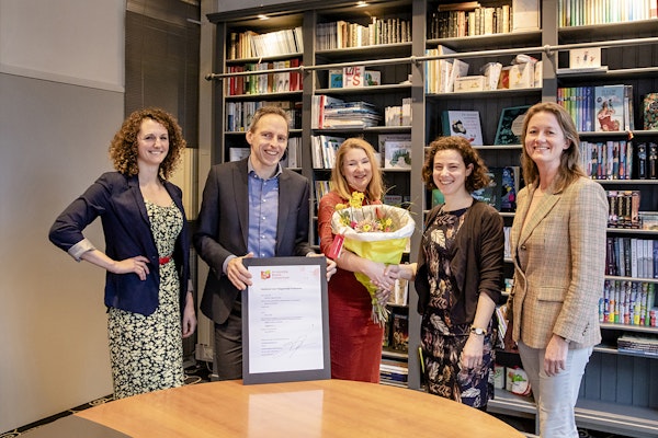 5 personen voor een boekenkast met bloemetje en ondertekend document