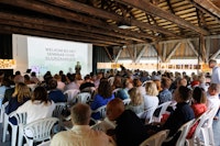 Zaal met mensen die op stoeltjes zitten te kijken naar een man die voor een scherm staat waarop staat 'welkom bij het seminar over duurzaamheid'.