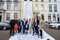 11 personen staande op een meterslange 'kassabon' die aan een gebouw naar beneden hangt