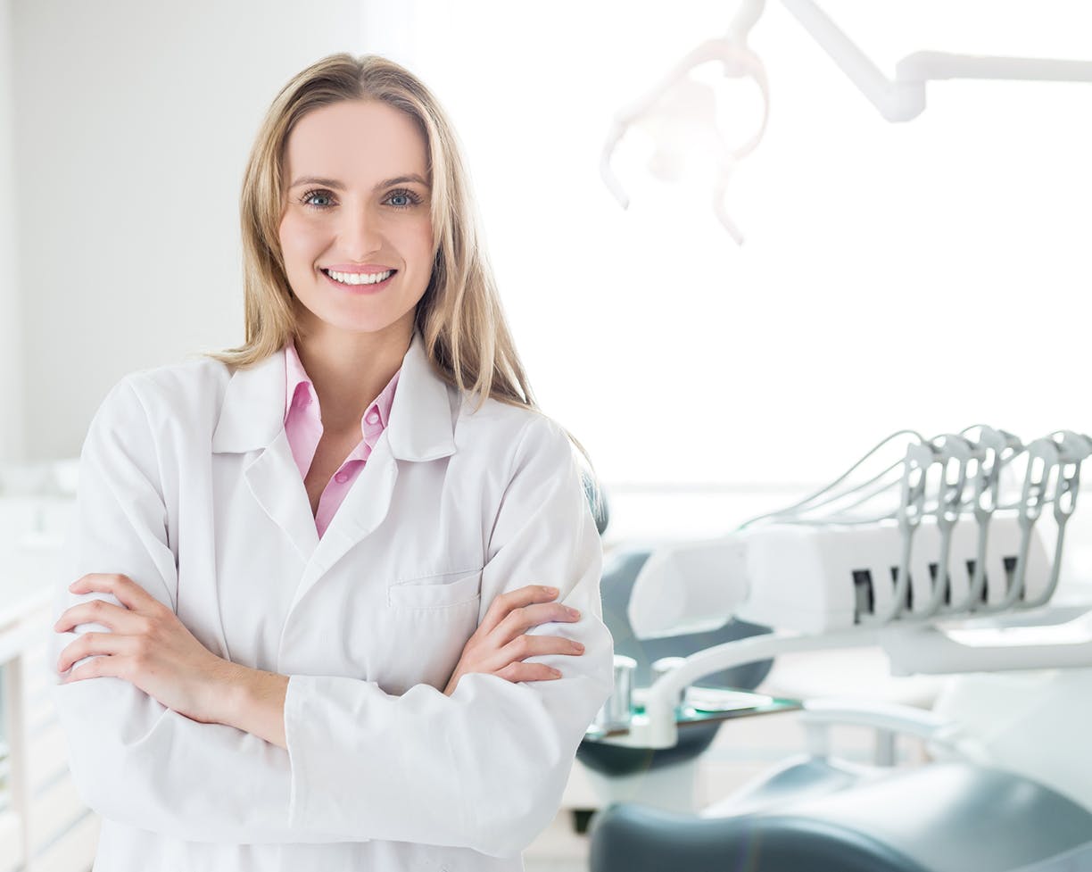 A woman in a lab coat with her arms crossed smiling