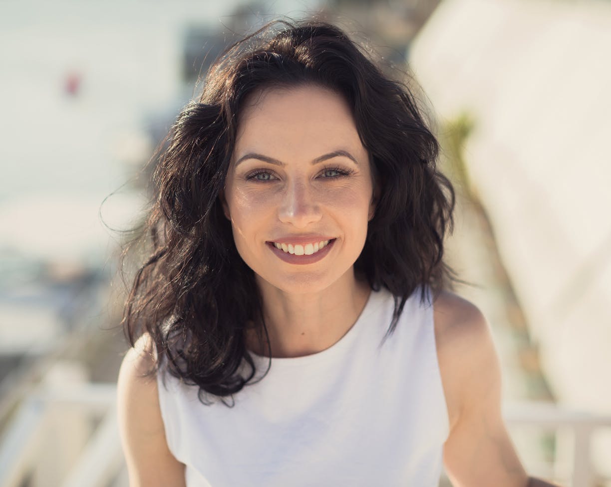 Dark-haired woman in a white shirt smiling outside