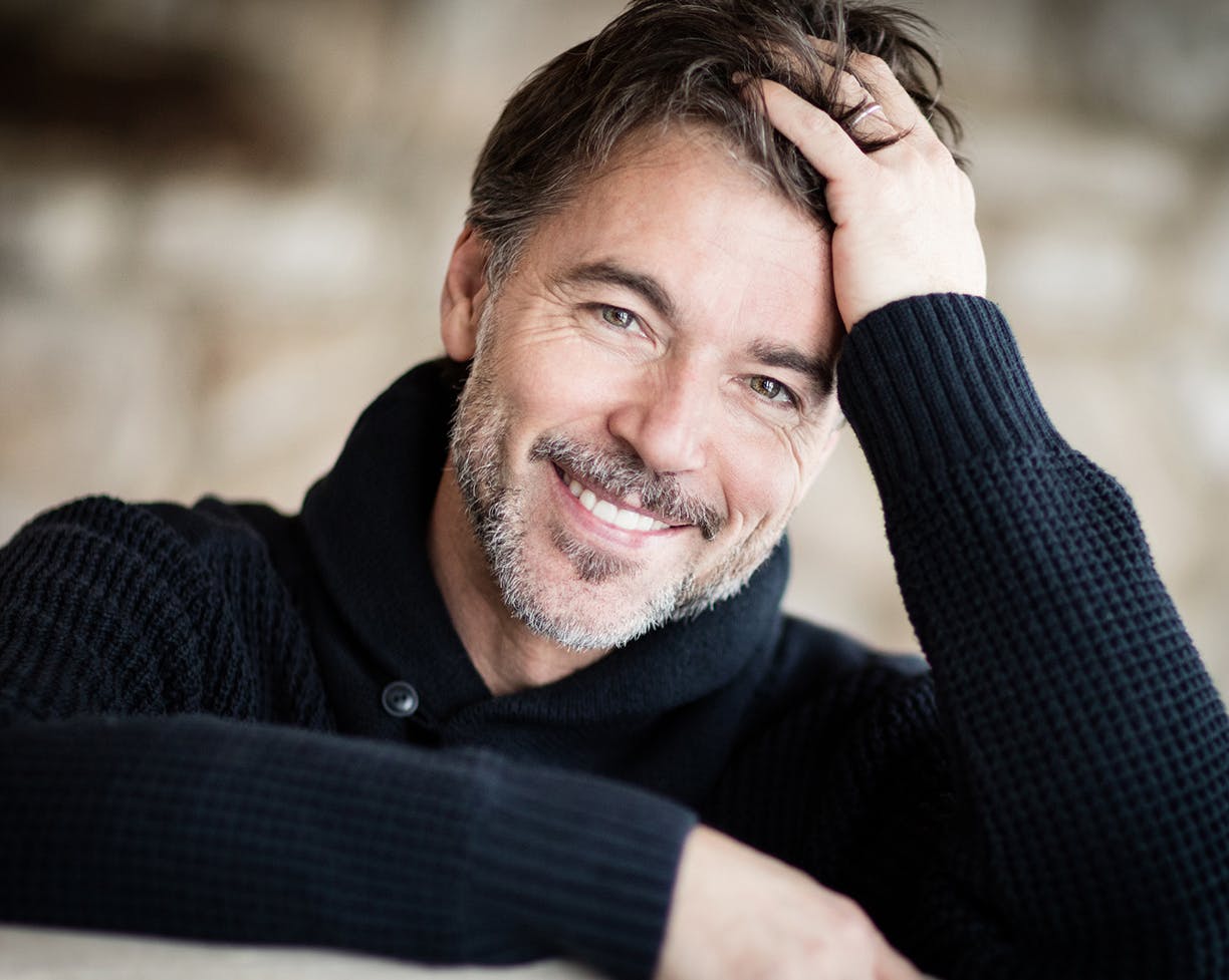 Man in a black sweater holding his head in his hand