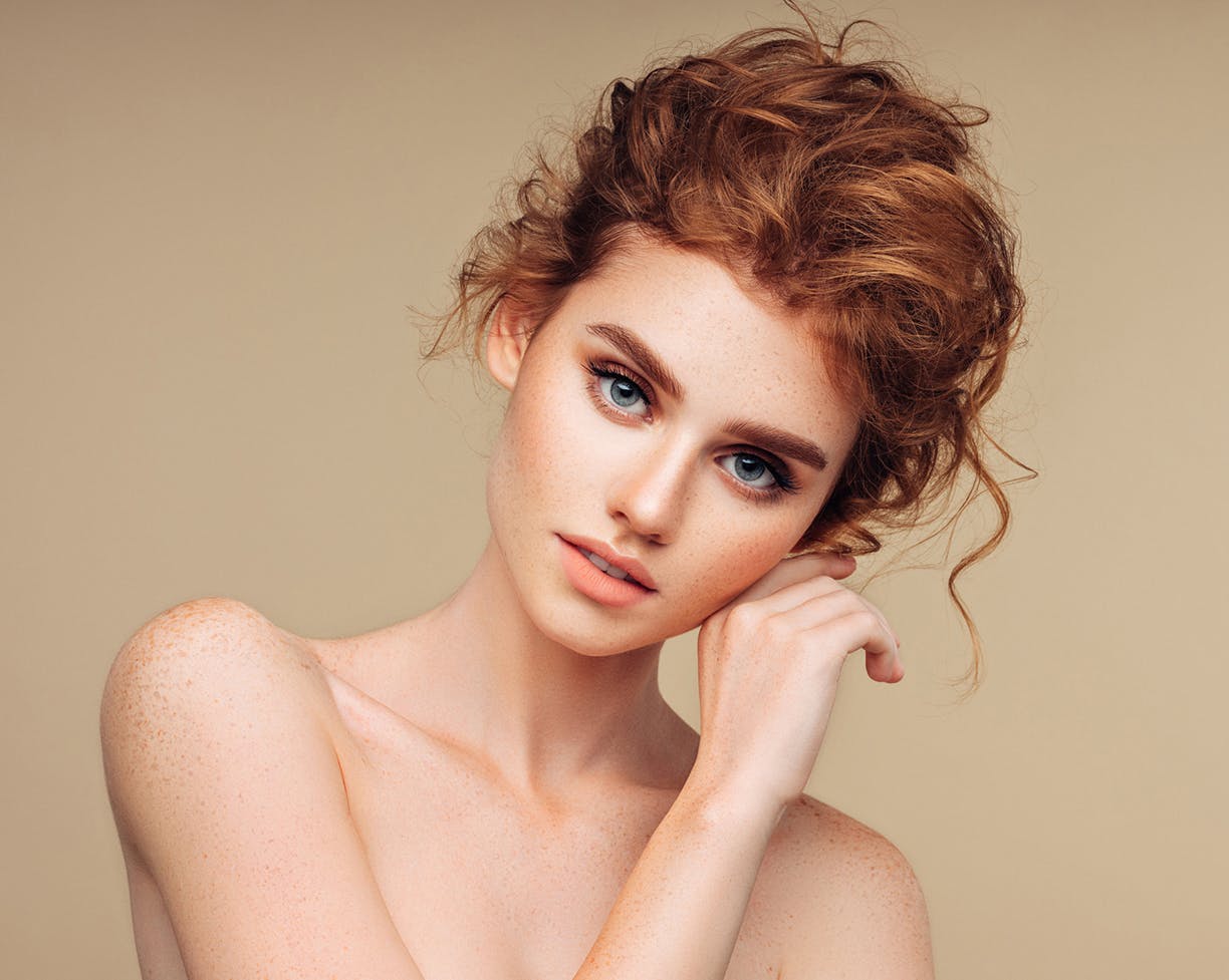 Red-headed woman who is shirtless touching her ear