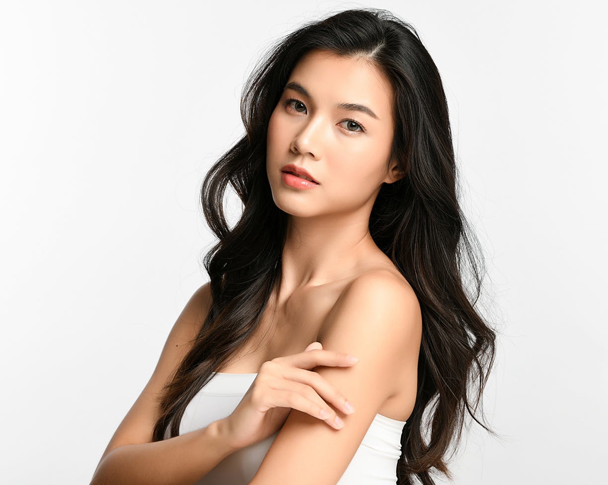 Woman with long black hair in a white top touching her arm