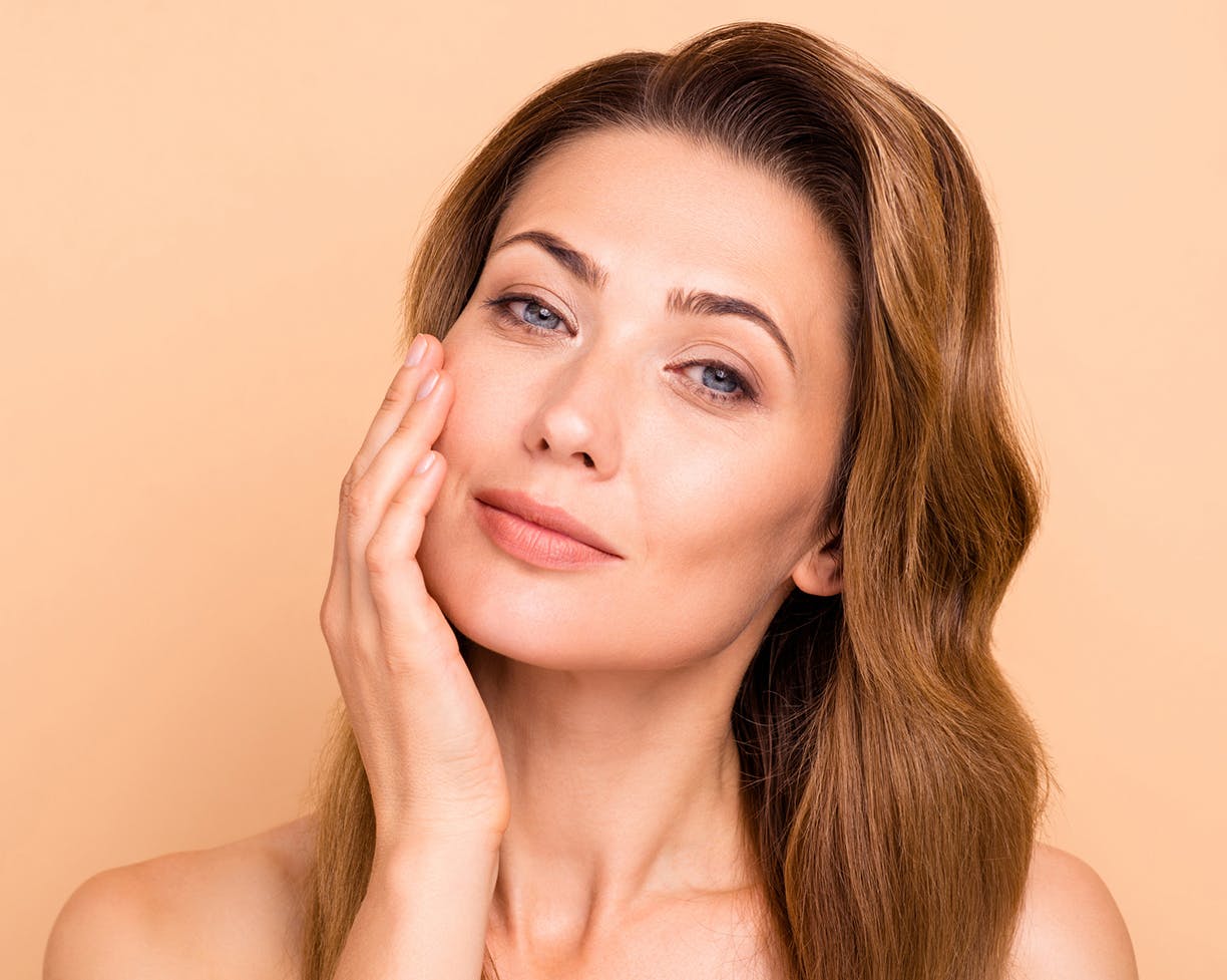 Woman holding her face in front of a neutral background