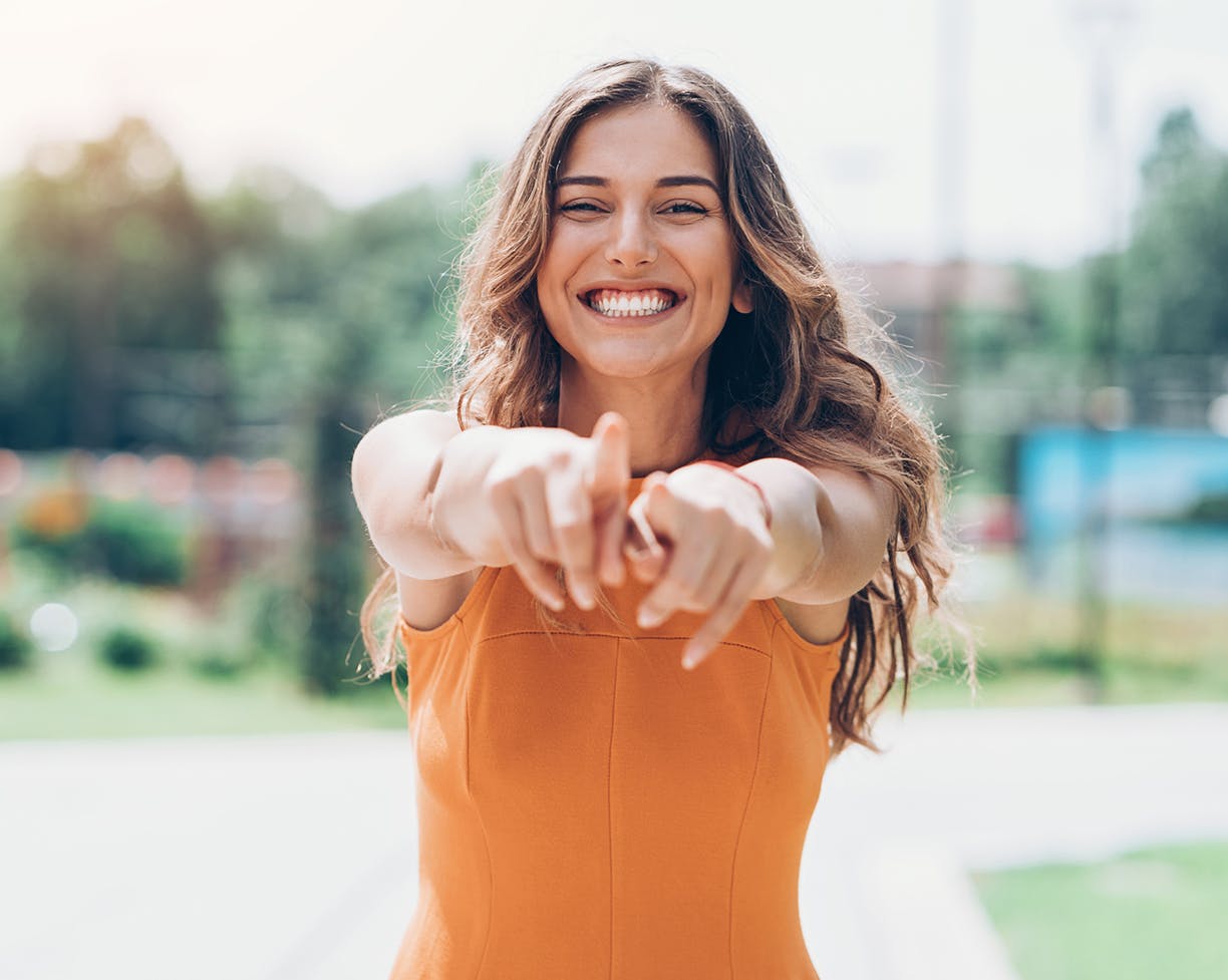 Woman in orange top pointing at camera smiling