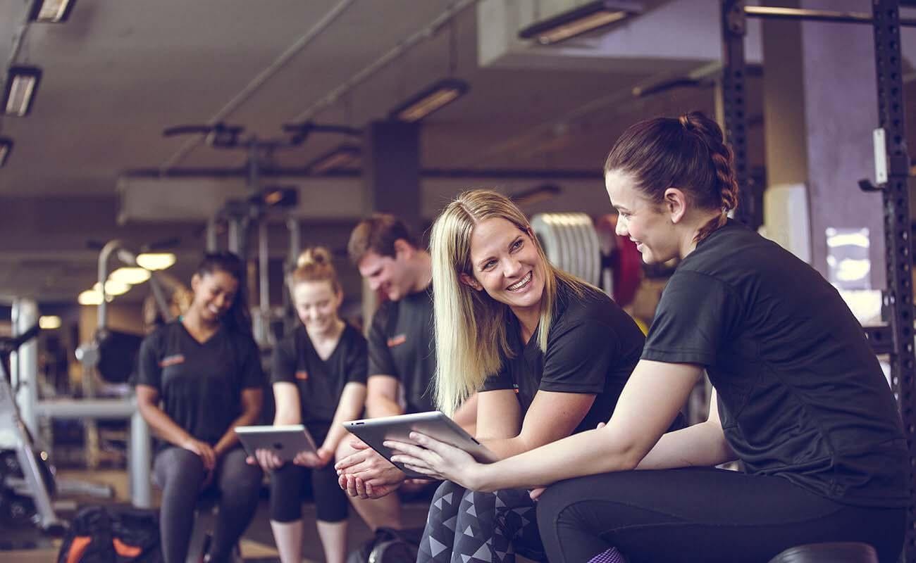 Five personal trainers seated together in discussion within a gym