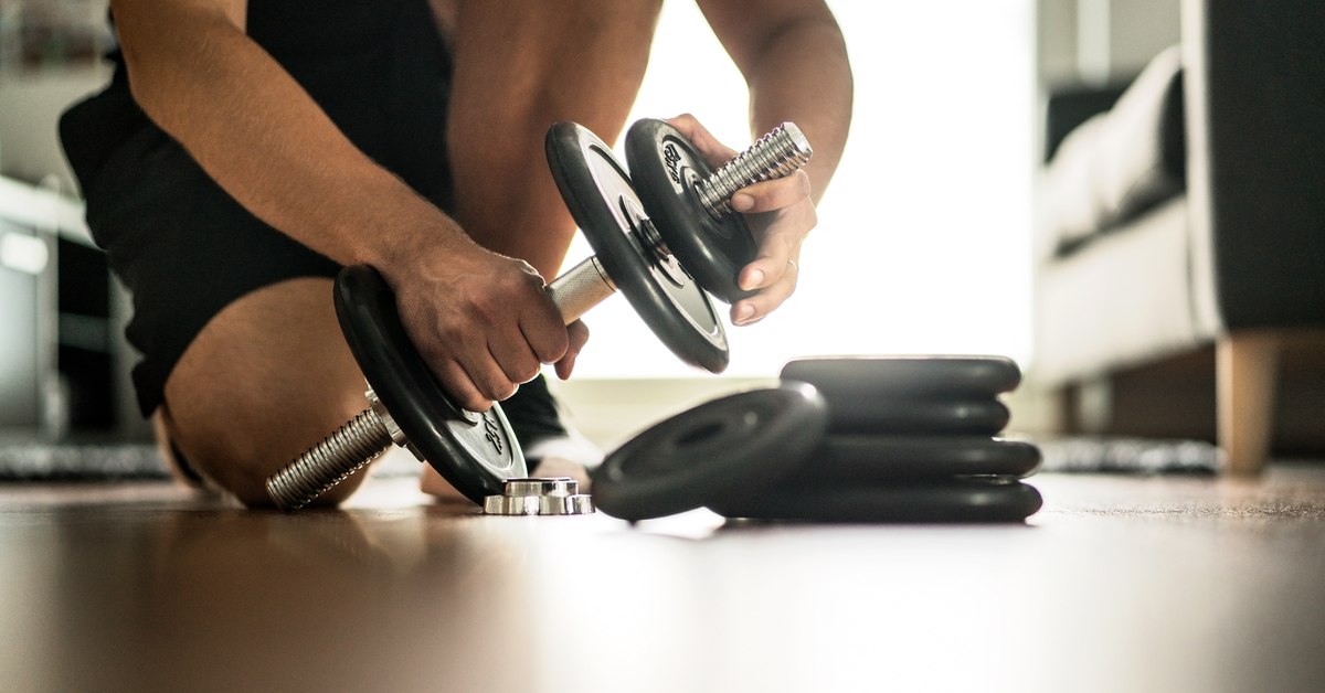 A man kneels as he adds weight to hand weights