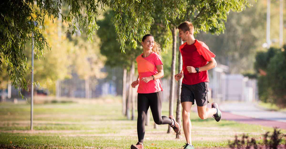 Male and female running next to each other and talking in the park