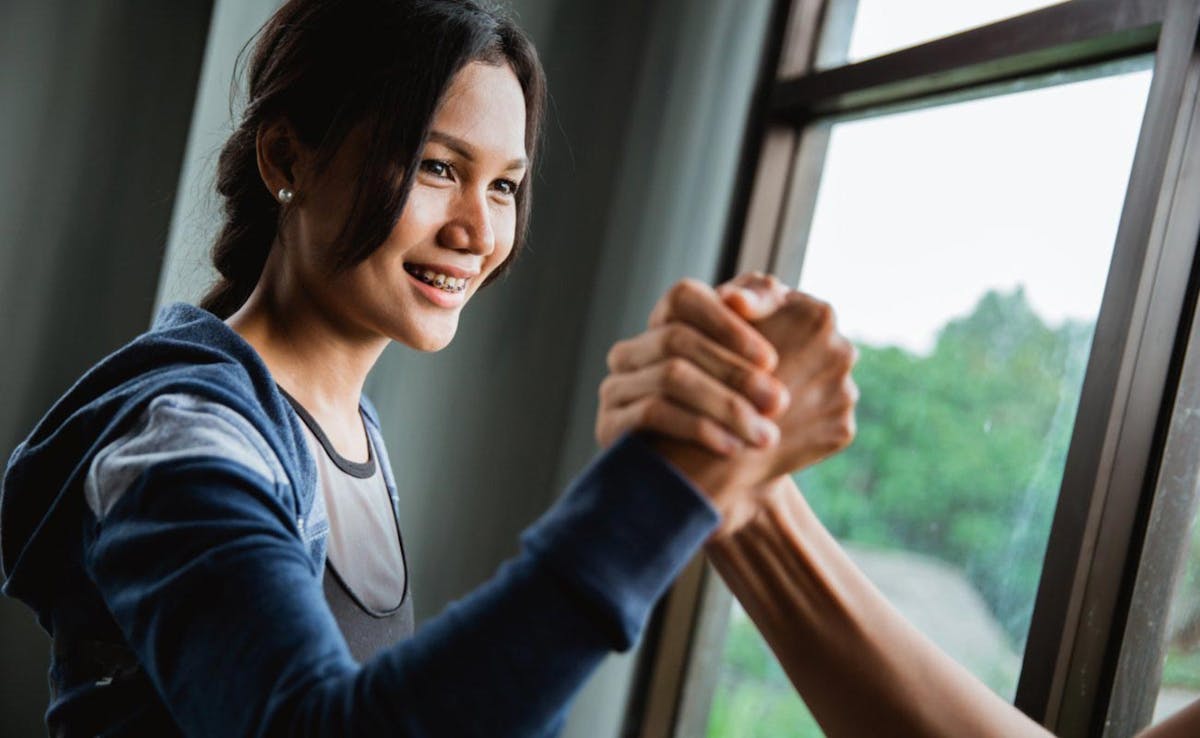 Woman arm wrestling with personal trainer in front of window