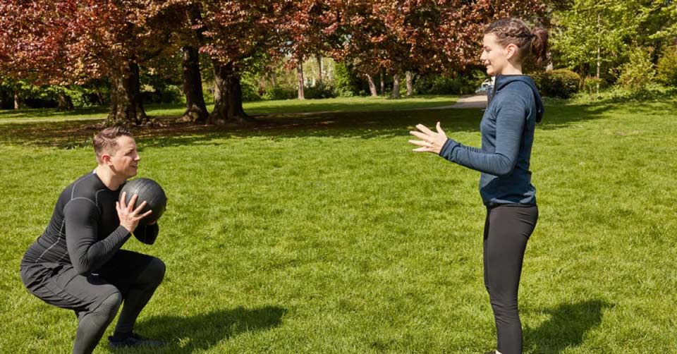 Man and women doing squat with medicine ball