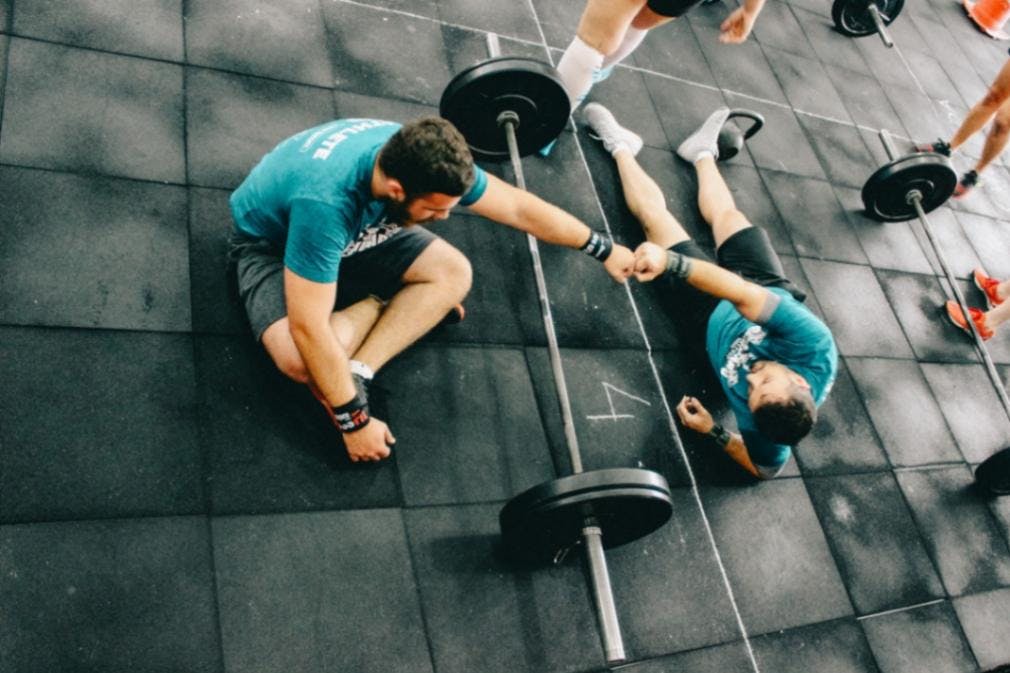 Two men lying on gym floor and fist bumping